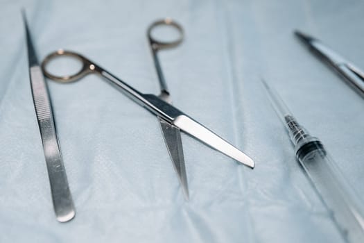Detailed view of surgical tools including scissors on a blue sterile surface.