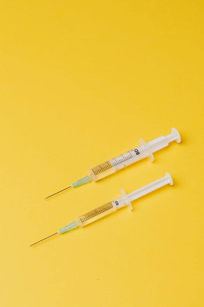 Two syringes on a yellow background, emphasizing medical and healthcare themes.